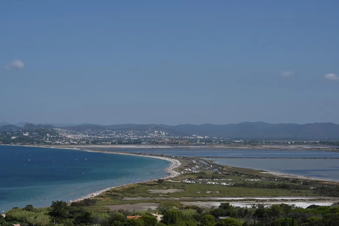 A wide-angle view captures the unique, narrow stretch of land that connects the peninsula of Hyères to the mainland, creating a salt marsh on one side and a beach on the other.
