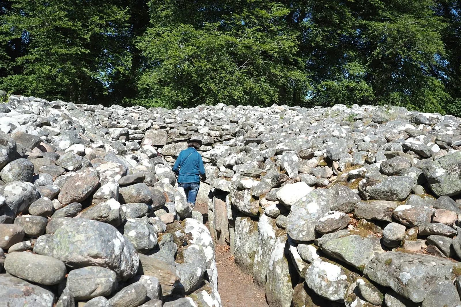 A person walks through the historic Clava Cairns, a Bronze Age cemetery with large stone rings and burial mounds.