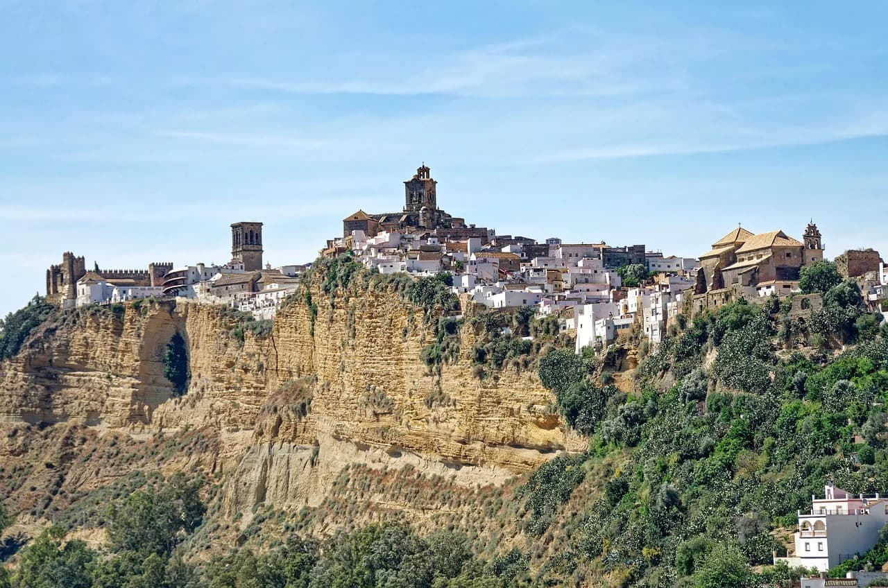 The picturesque white town of Arcos de la Frontera sits atop a dramatic cliff, with a castle and a church overlooking the valley.