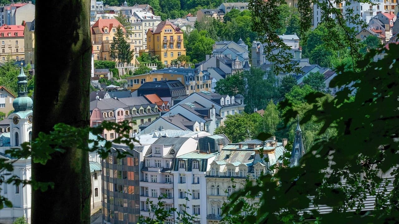 The colorful rooftops and spires of Karlovy Vary are nestled within a green, forested landscape.