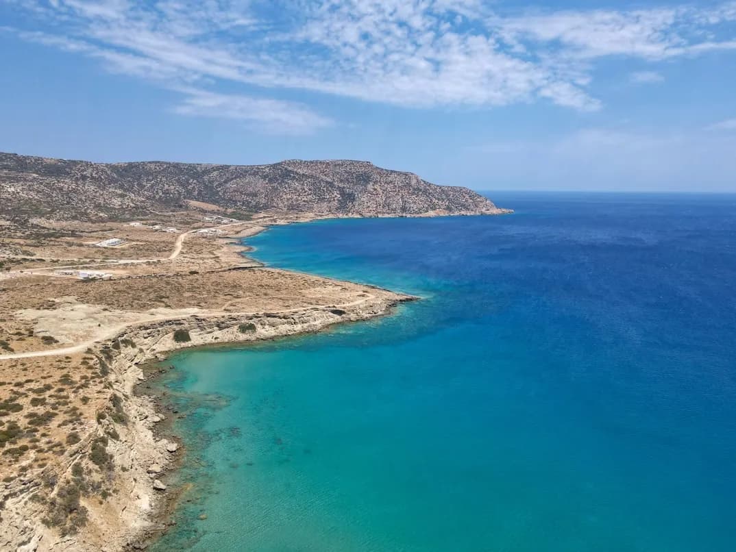 The stunning turquoise waters of Karpathos meet a rugged, rocky coastline, with a winding road tracing the landscape.