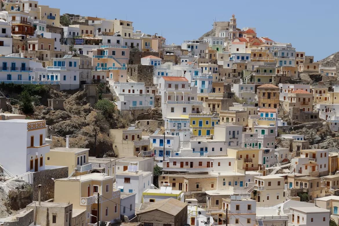 The traditional, colorful houses of a village on the island of Karpathos are built into a steep, rocky hillside.