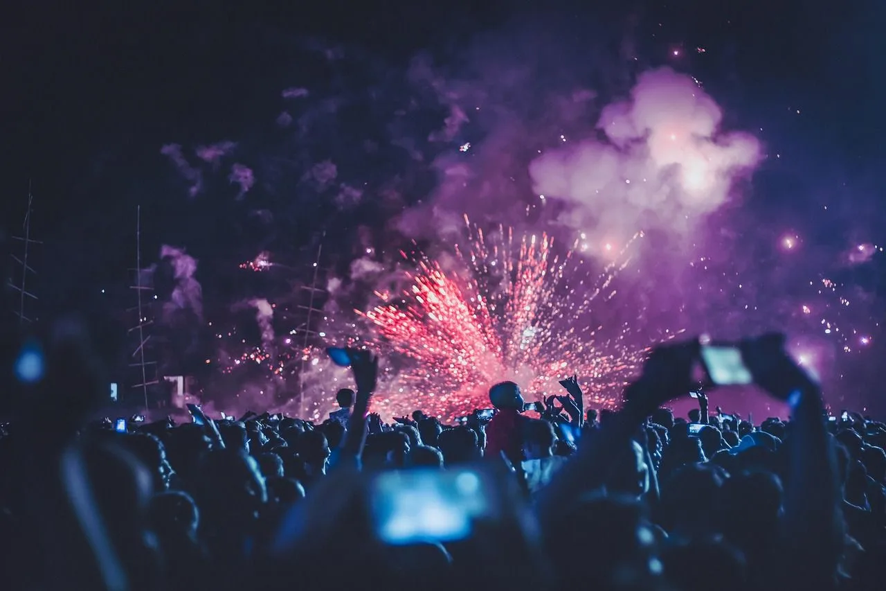 A crowd of people watches a fireworks display in the night sky, with a festive atmosphere.