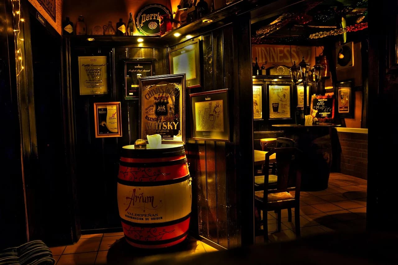 The cozy and dimly lit interior of a traditional Irish pub, with wooden barrels, framed pictures, and various beer signs.