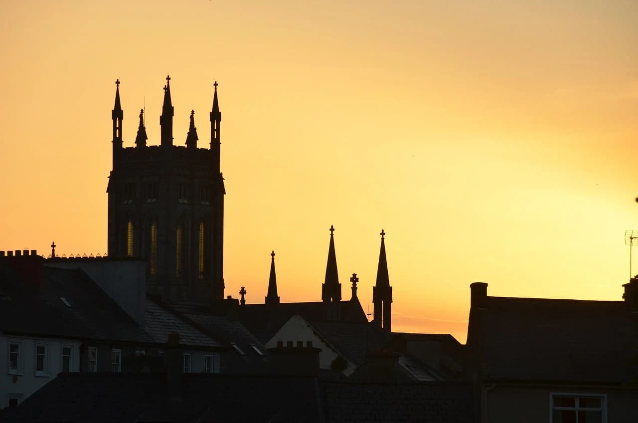 The silhouetted spires of St. Canice's Cathedral are a dramatic sight against a vibrant orange and yellow sunset.