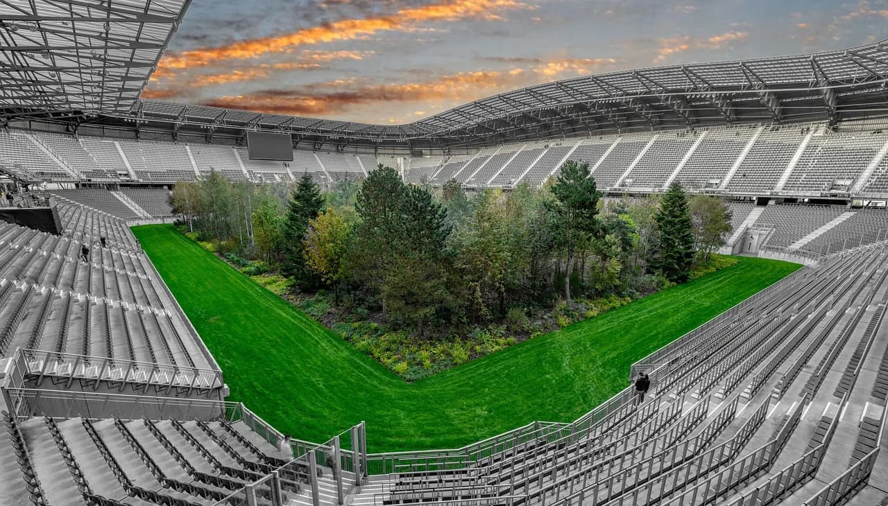 A surreal art installation features a green forest in the middle of a large, empty stadium.