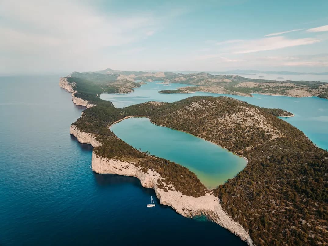 An aerial view captures the unique U-shaped bay of Telascica Nature Park, surrounded by dramatic cliffs and green landscape.