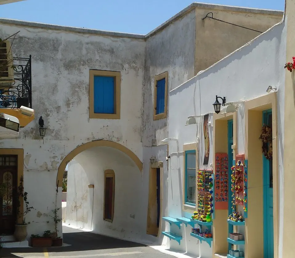 A narrow, arch-covered street with bright blue windows and white walls creates a charming scene in a traditional Greek village.
