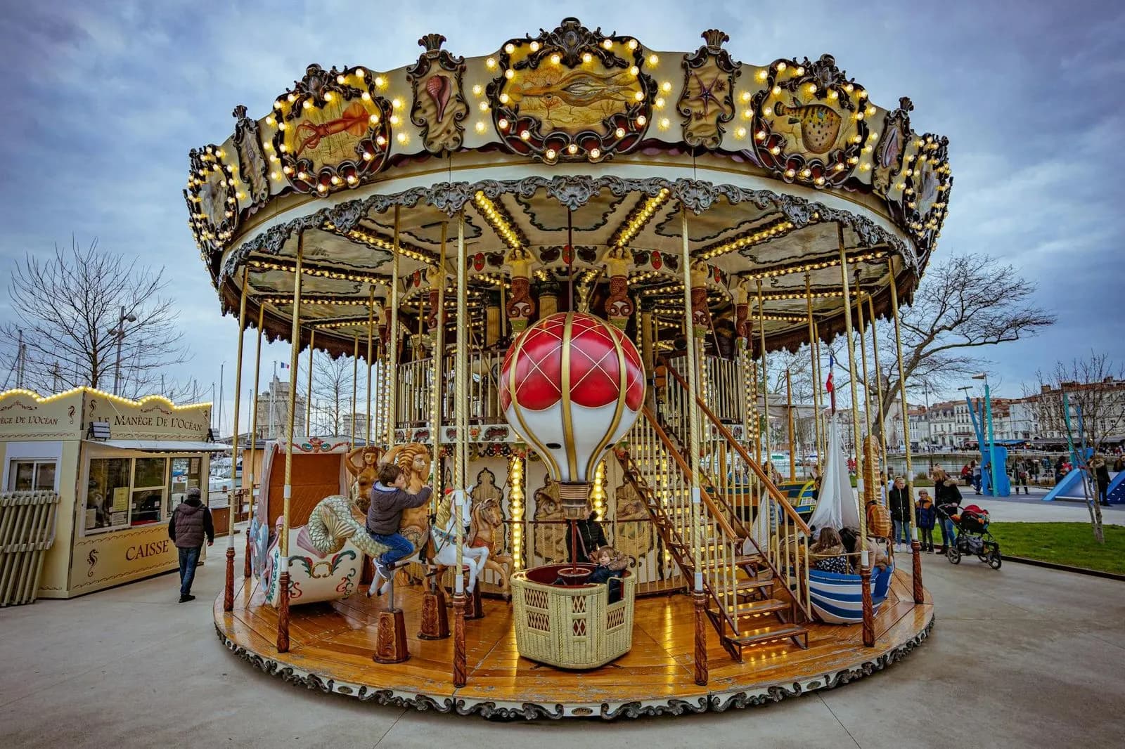 A vintage-style carousel with ornate horses and a hot air balloon provides a whimsical focal point near the historic harbor.