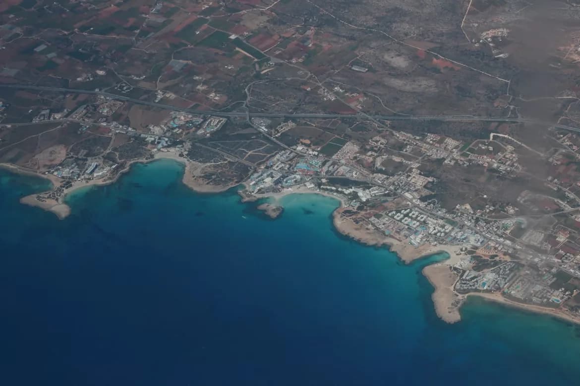 An aerial view captures the coastline, with residential buildings and hotels lining a series of sandy beaches and coves.