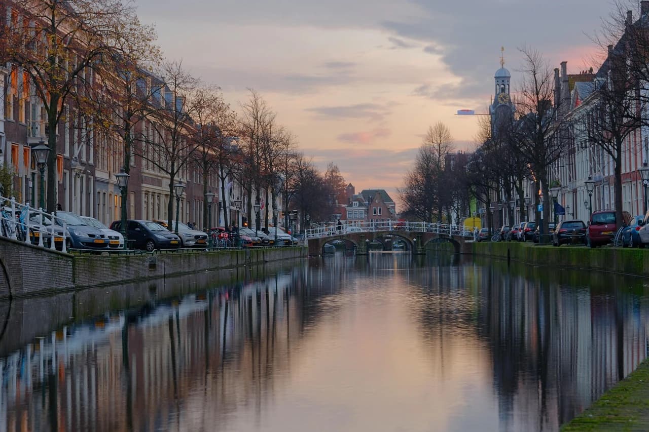 The serene canals of Leiden are beautifully reflected in the water, with charming bridges and classic architecture lining the banks at dusk.