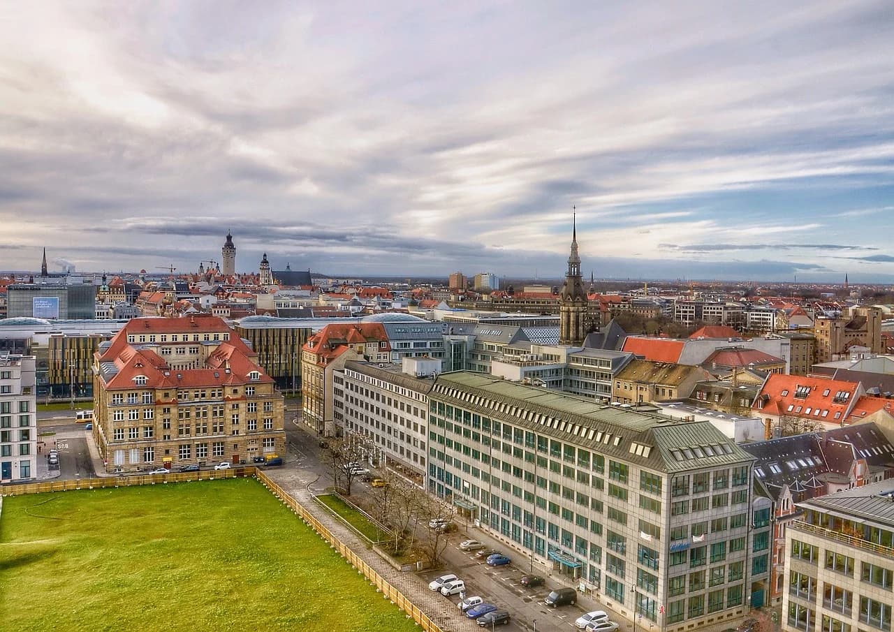 A panoramic view of Leipzig shows a mix of historic and modern buildings, with church spires and towers dominating the skyline.