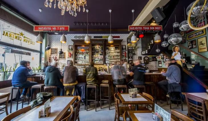 The cozy and vibrant interior of a local bar shows people relaxing at the counter and tables, capturing Leuven's famous pub culture.