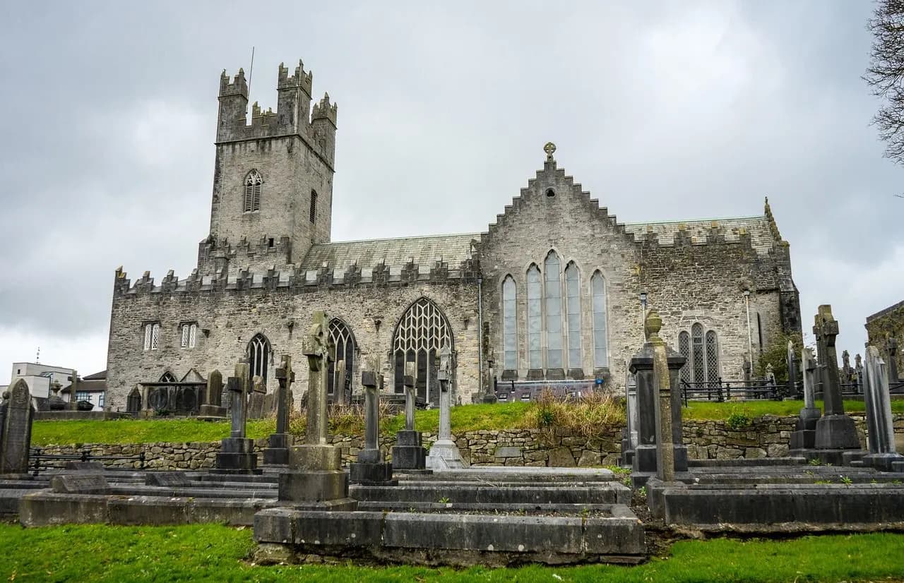 A historic stone church with a square tower and intricate stonework is set within a graveyard with traditional Irish Celtic crosses.