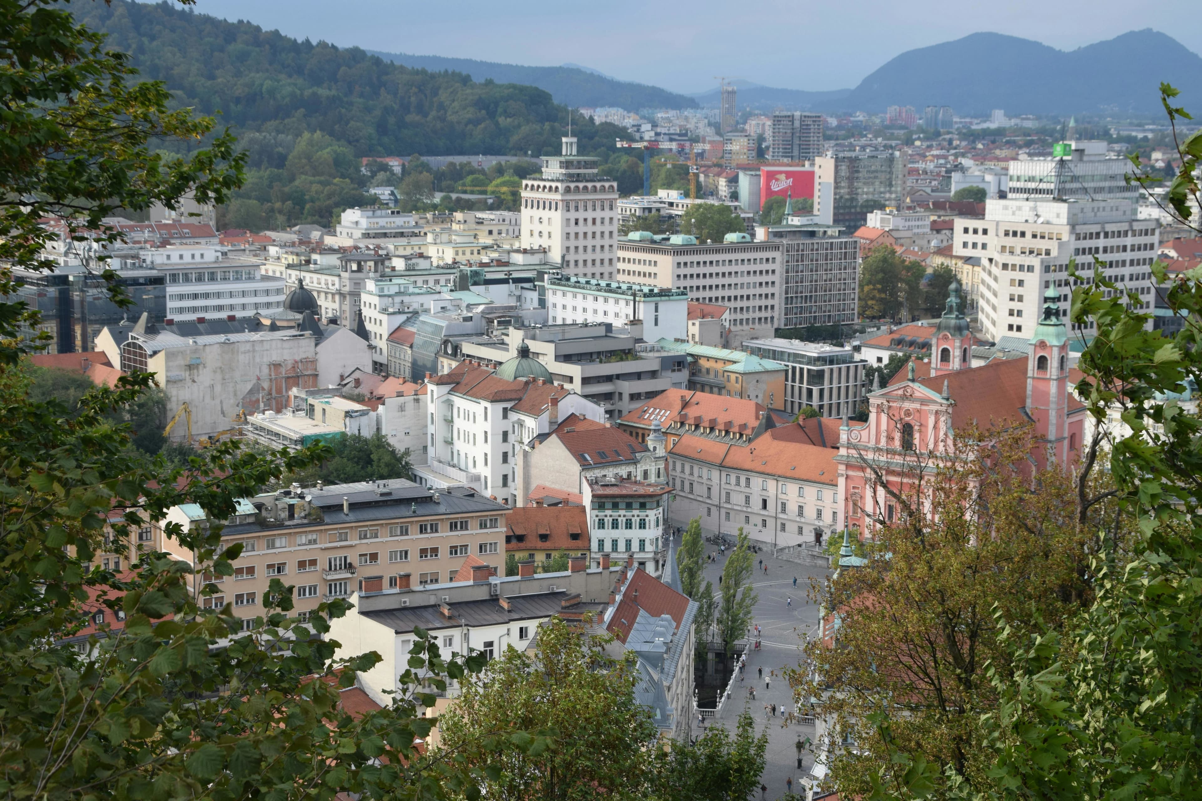A high-angle view captures the dense rooftops and buildings of Ljubljana's city center, with green hills in the distance.