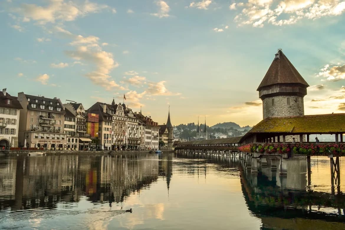 The historic Chapel Bridge, a famous landmark of Lucerne, is beautifully reflected in the tranquil waters of the Reuss River at sunset.