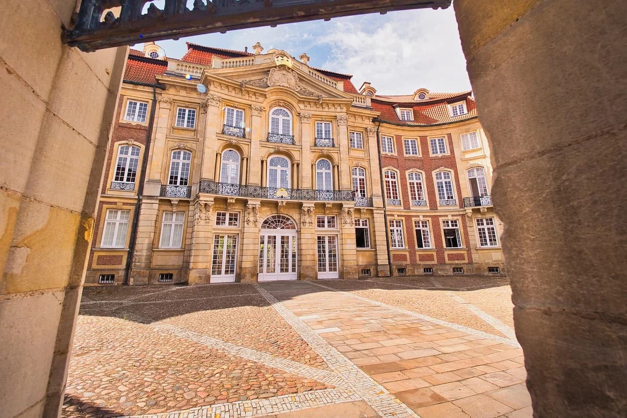 The ornate facade of a historic building, with its curved roof and large windows, is framed by a stone archway.