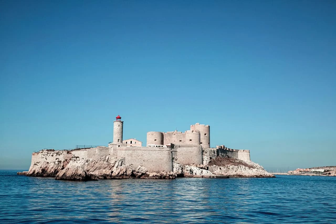 The historic Château d'If, a fortress on a small island, sits in the middle of the sea under a clear blue sky.