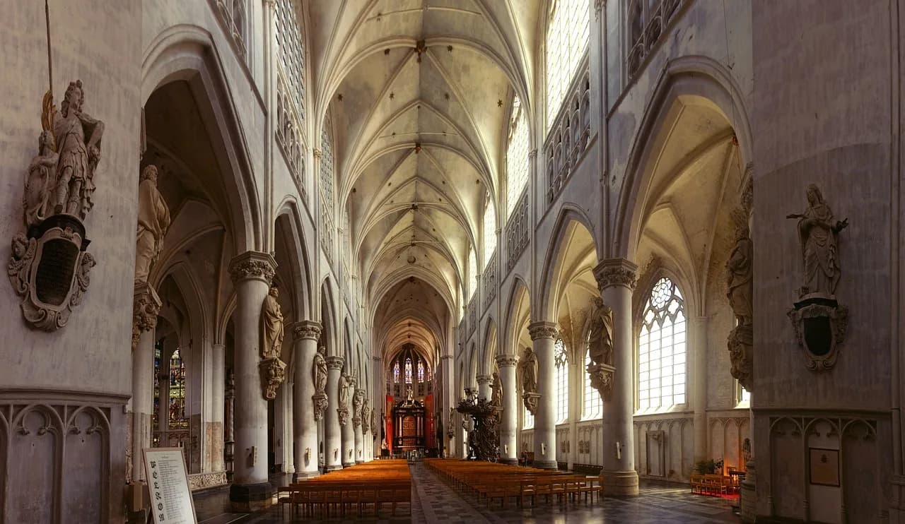 The grand, vaulted interior of a cathedral with a long nave, numerous arches, and stained glass windows.