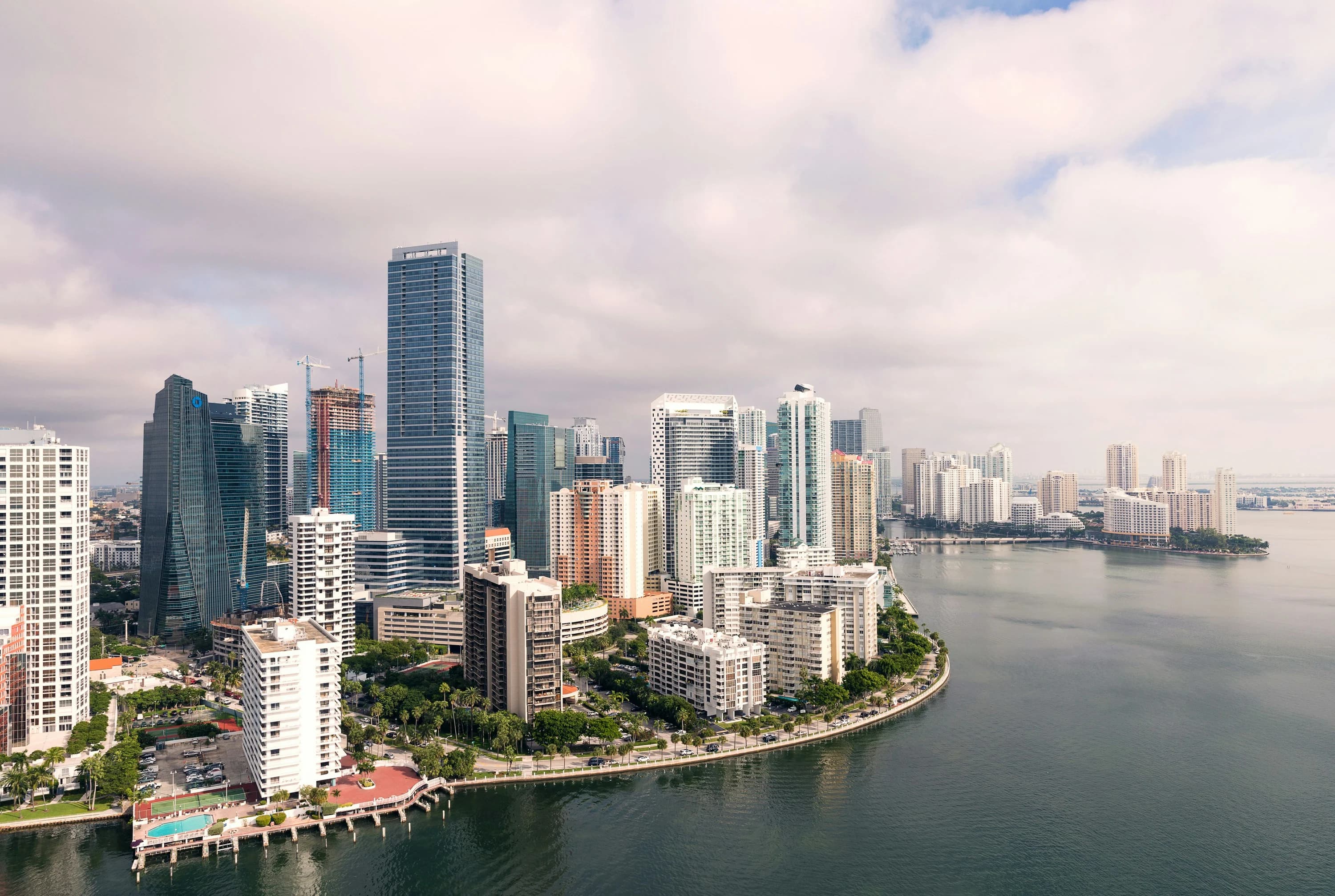 A panoramic view captures the dense urban landscape of Miami, with a line of modern skyscrapers and the sea stretching to the horizon.