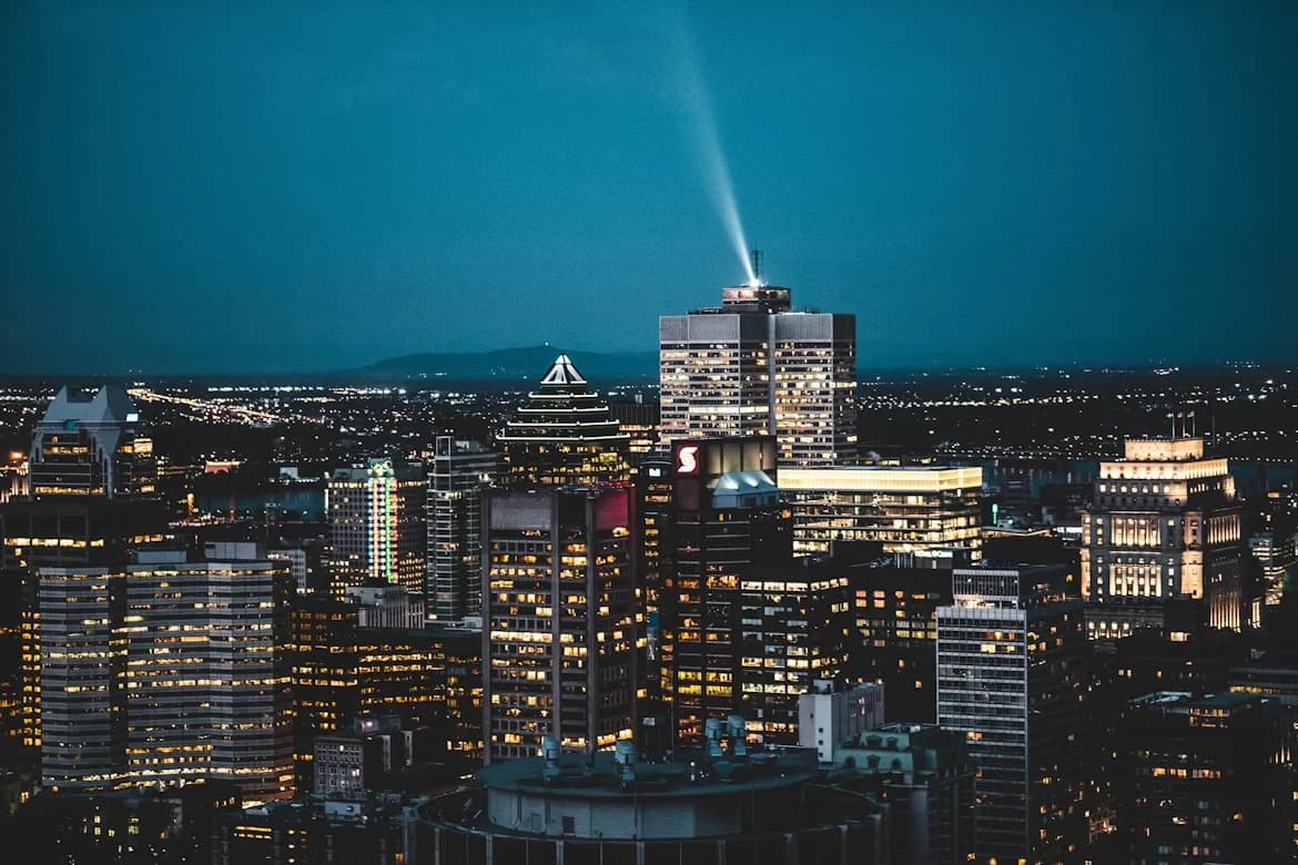 A panoramic view of the Montreal skyline at dusk, with a unique building with a light beam shooting into the sky.