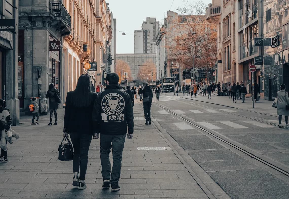 A couple walks down a busy city street in Nancy, with traditional buildings and cafes on either side.