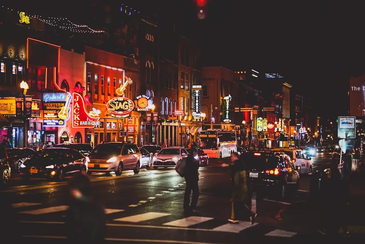 The bustling streets of Nashville are illuminated at night by neon signs from numerous bars and music venues.