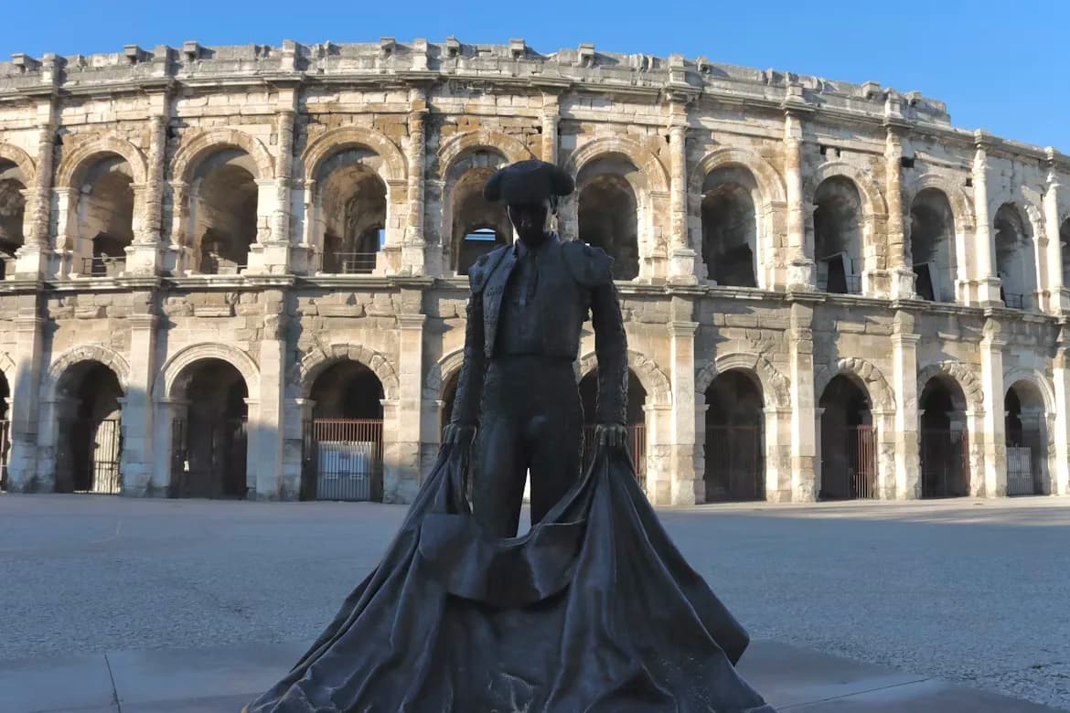 A statue of a matador holding a red cape stands in front of the Roman Amphitheater of Nîmes, a popular spot for bullfighting.