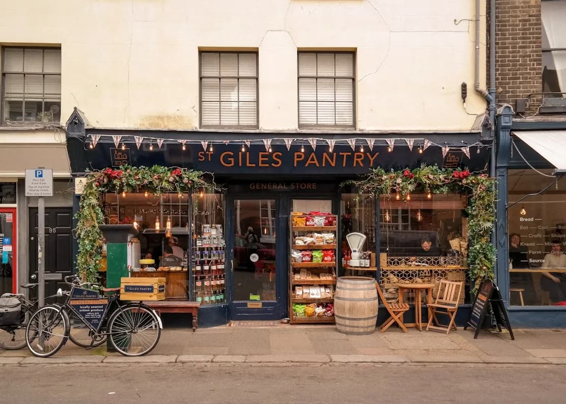 A traditional English storefront with a sign that says "St Giles Pantry" is decorated with festive garlands and lights.