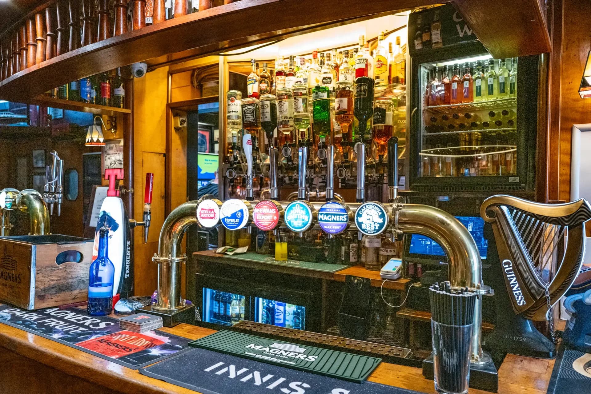 The interior of a traditional Scottish pub features a large wooden bar with numerous beer taps and a selection of spirits.