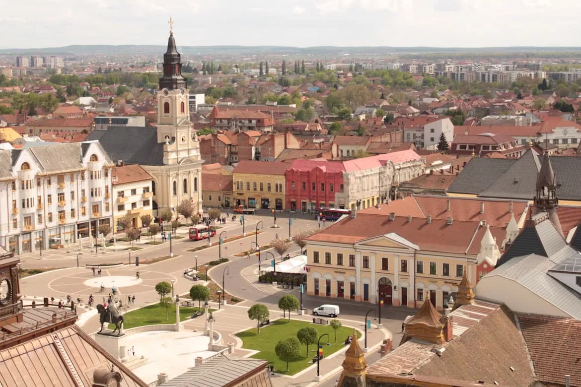 A high-angle view captures the city of Oradea, with its mix of historic and modern buildings and a large city square in the foreground.