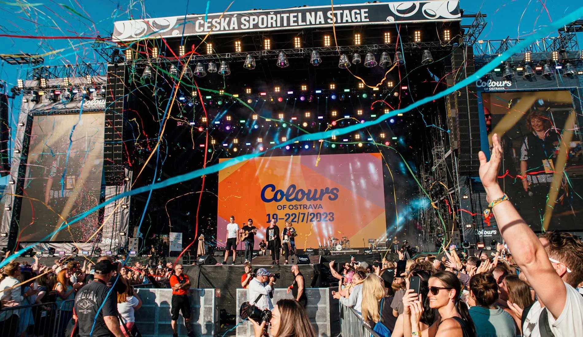 A live band performs on a large stage at the Colours of Ostrava music festival, with a crowd of people in the foreground.