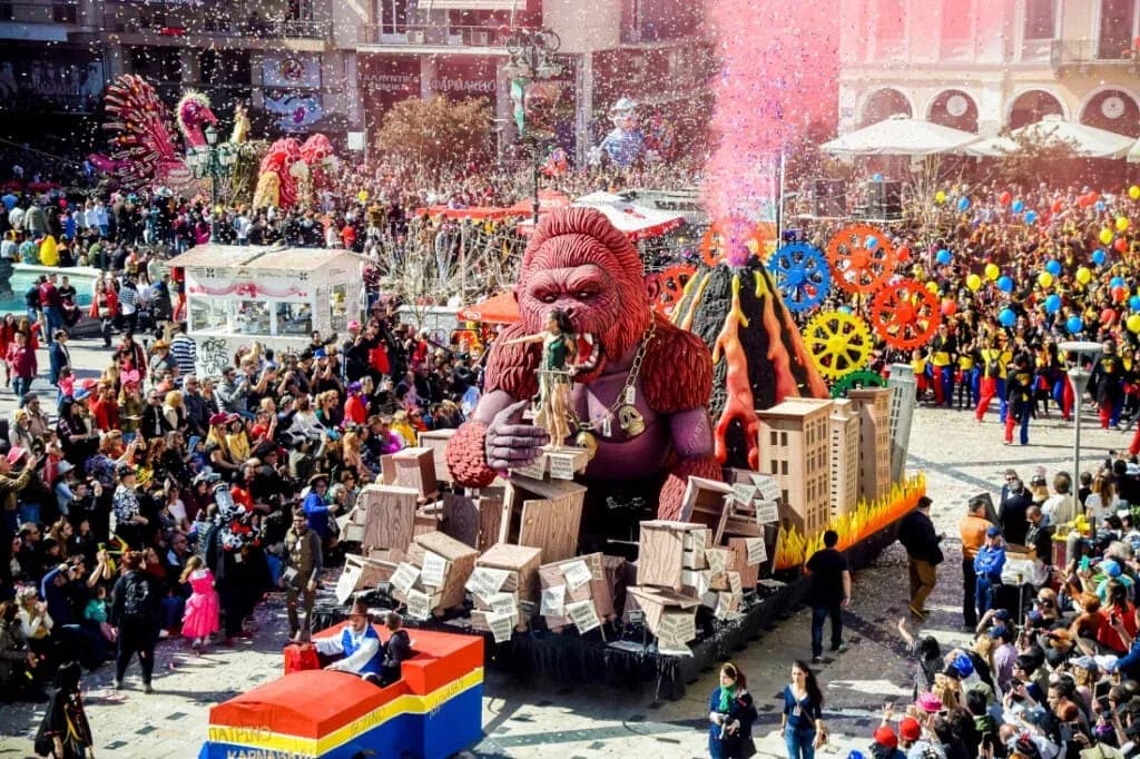 A large carnival float of a giant, red gorilla is the centerpiece of a festive parade, with a crowd of people in the background.