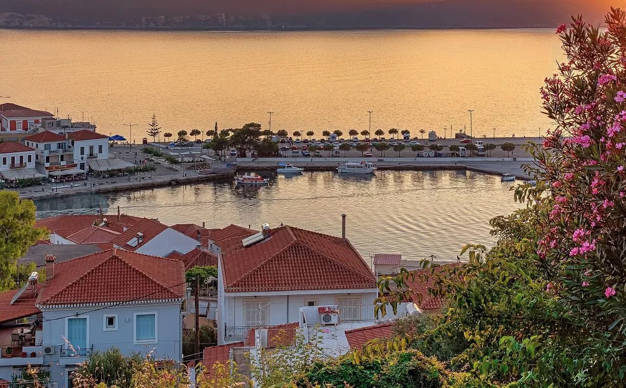 A peaceful harbor is filled with boats, with the traditional houses of a seaside town and a stunning sunset in the background.