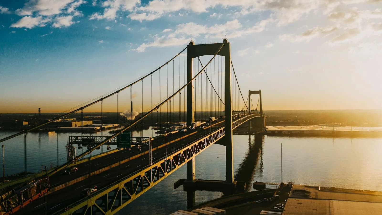 The impressive Benjamin Franklin Bridge spans a wide river at sunset, connecting the cities on either side.