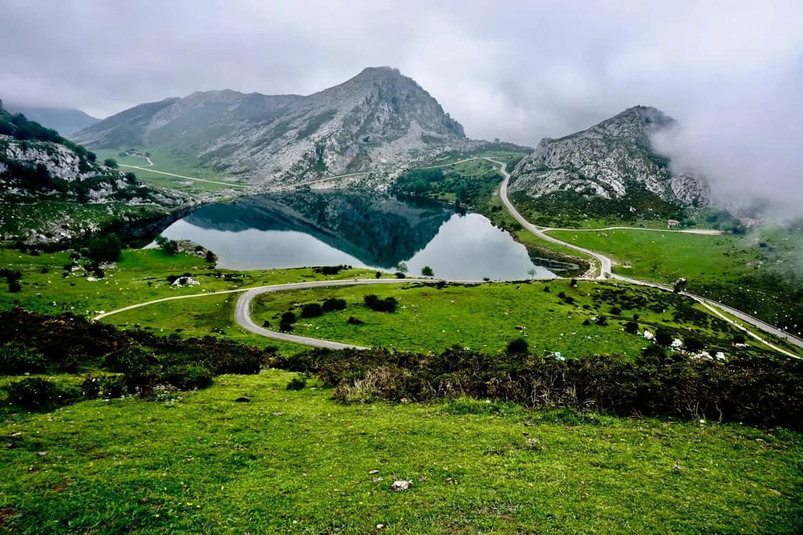 The stunning Covadonga Lakes are nestled in a green valley, with a road winding around the hills.