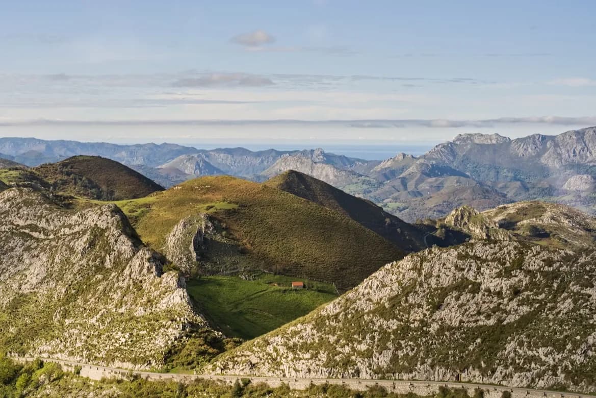 The green, rolling hills and valleys of the Picos de Europa mountains stretch to the horizon, with the sea visible in the distance.