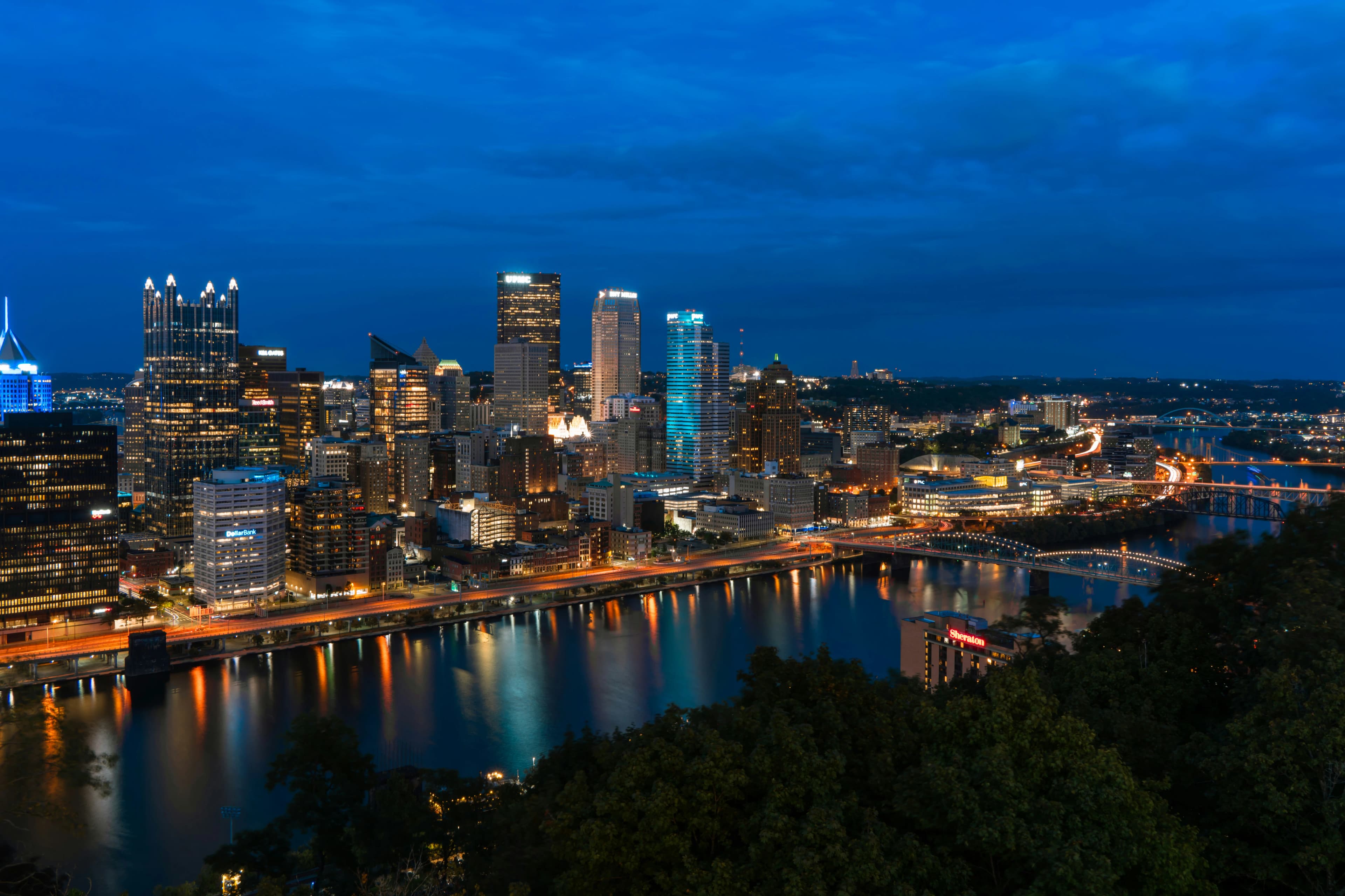 A historic trolley with a "Downtown" sign is seen on a street, with modern buildings and trees in the background.