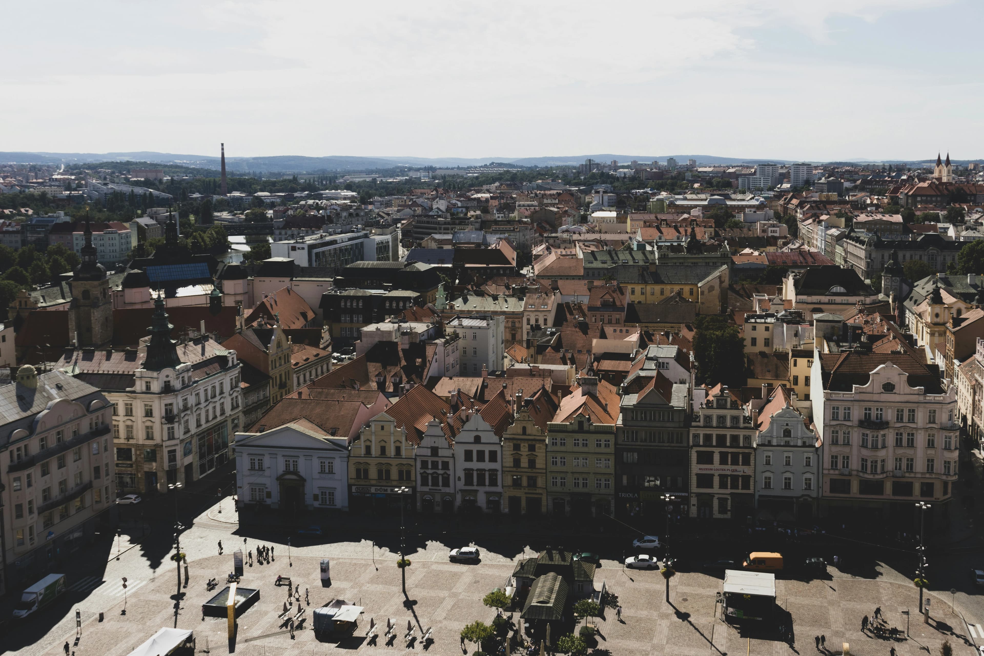 A panoramic view captures the city of Plzeň, with its colorful historic buildings and a wide, open city square.