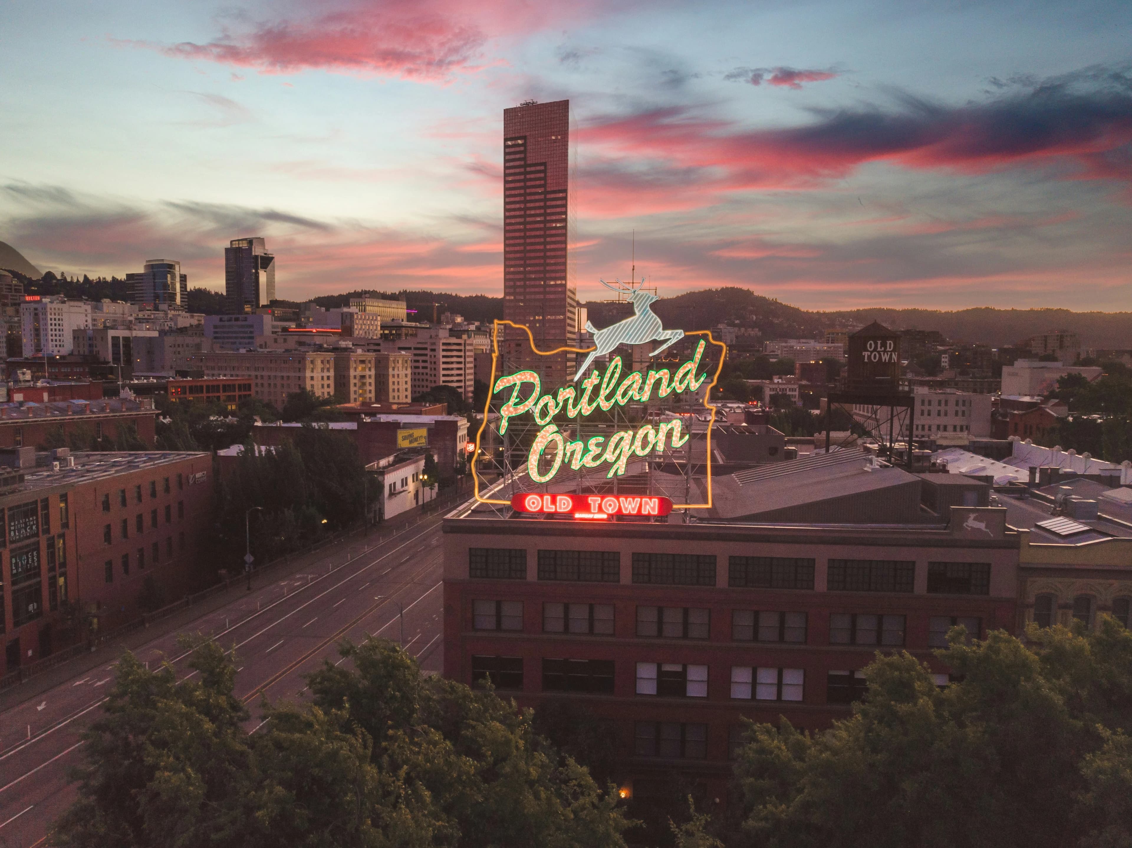 The iconic "White Stag" sign, a famous landmark of Portland, is a beautiful sight at dusk, with the city skyline in the background.