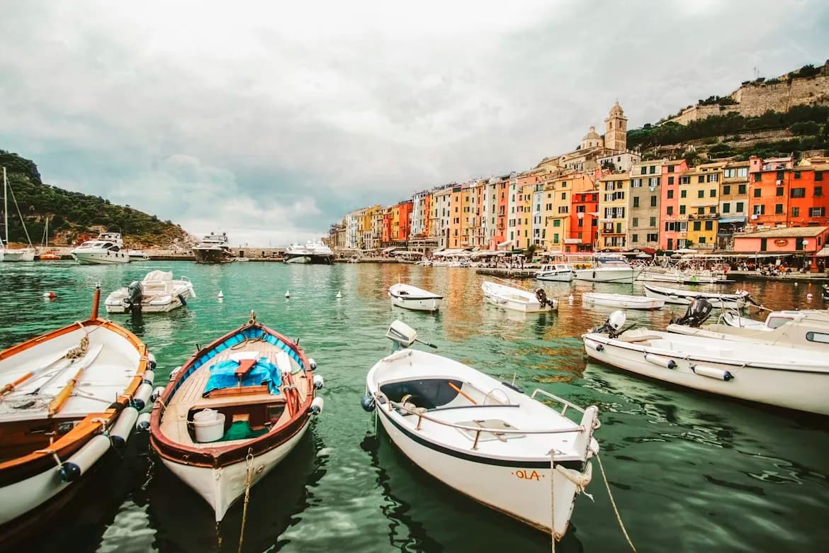 A variety of small boats are moored in the harbor of Portovenere, with the colorful facades of the city's buildings in the background.