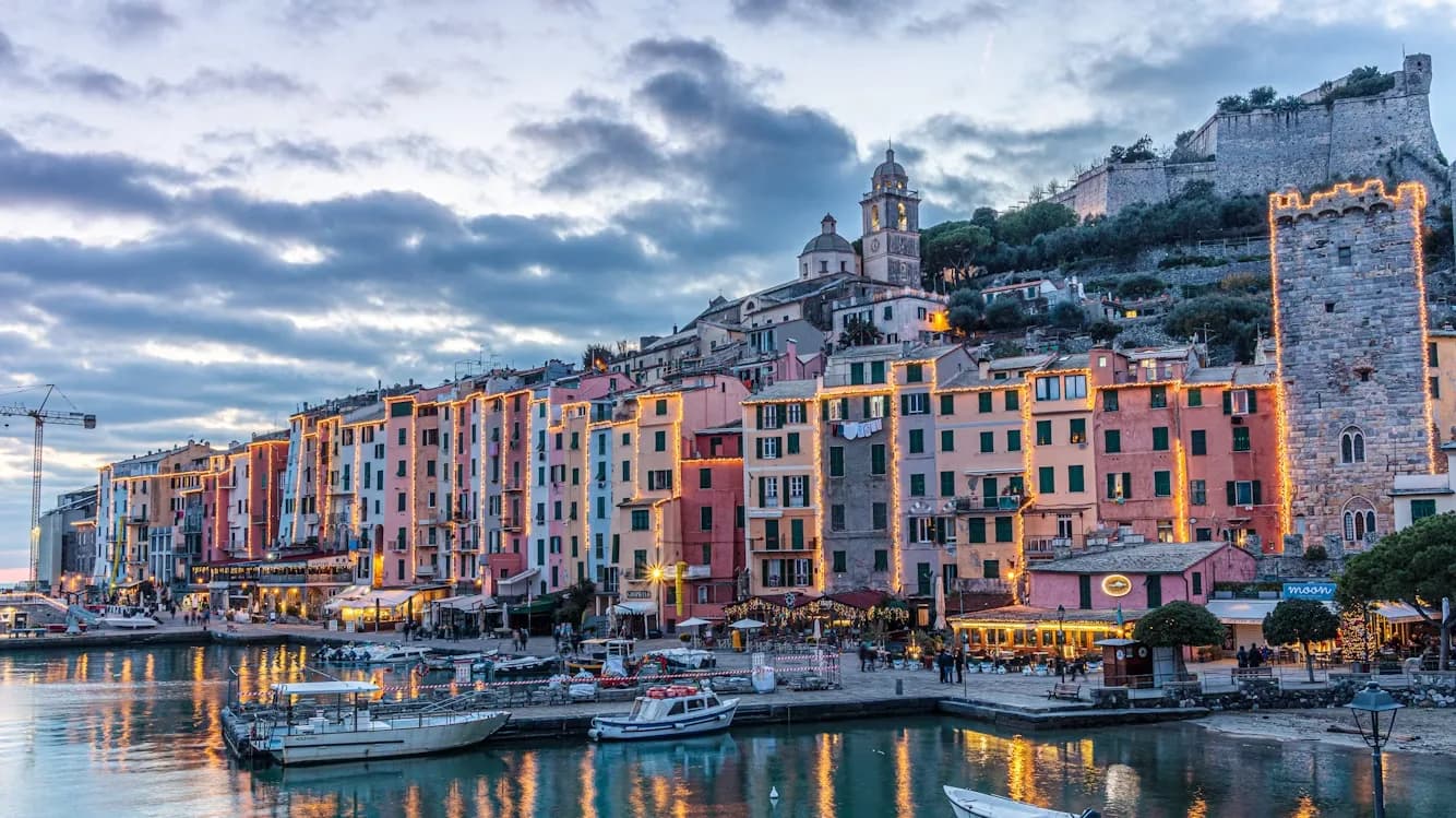 The colorful, traditional buildings of Portovenere's harbor are beautifully illuminated at night, with their lights reflecting on the calm water.