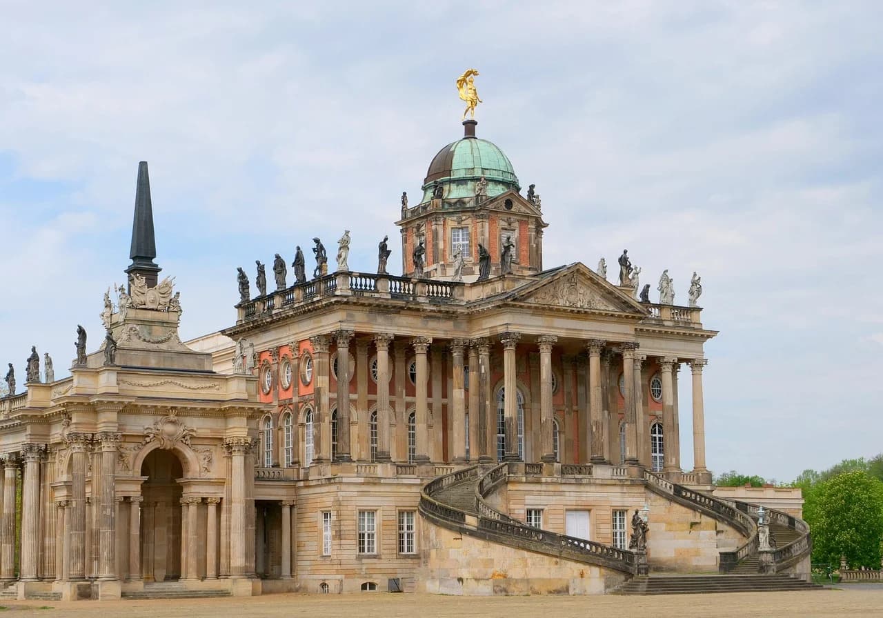 The magnificent Neues Palais, a grand baroque palace with a golden statue on top, is a highlight of the Sanssouci Park.