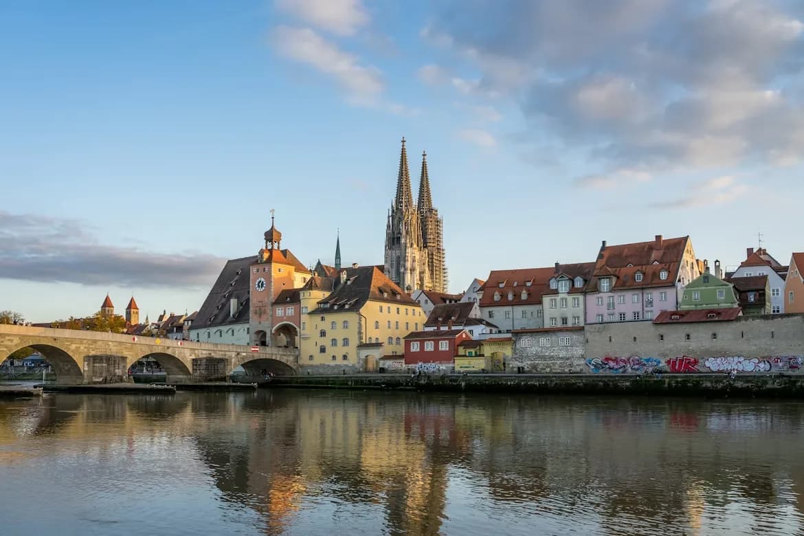The Steinerne Brücke, or Stone Bridge, with its numerous arches, crosses the Danube River, with the towers of St. Peter's Cathedral in the background.