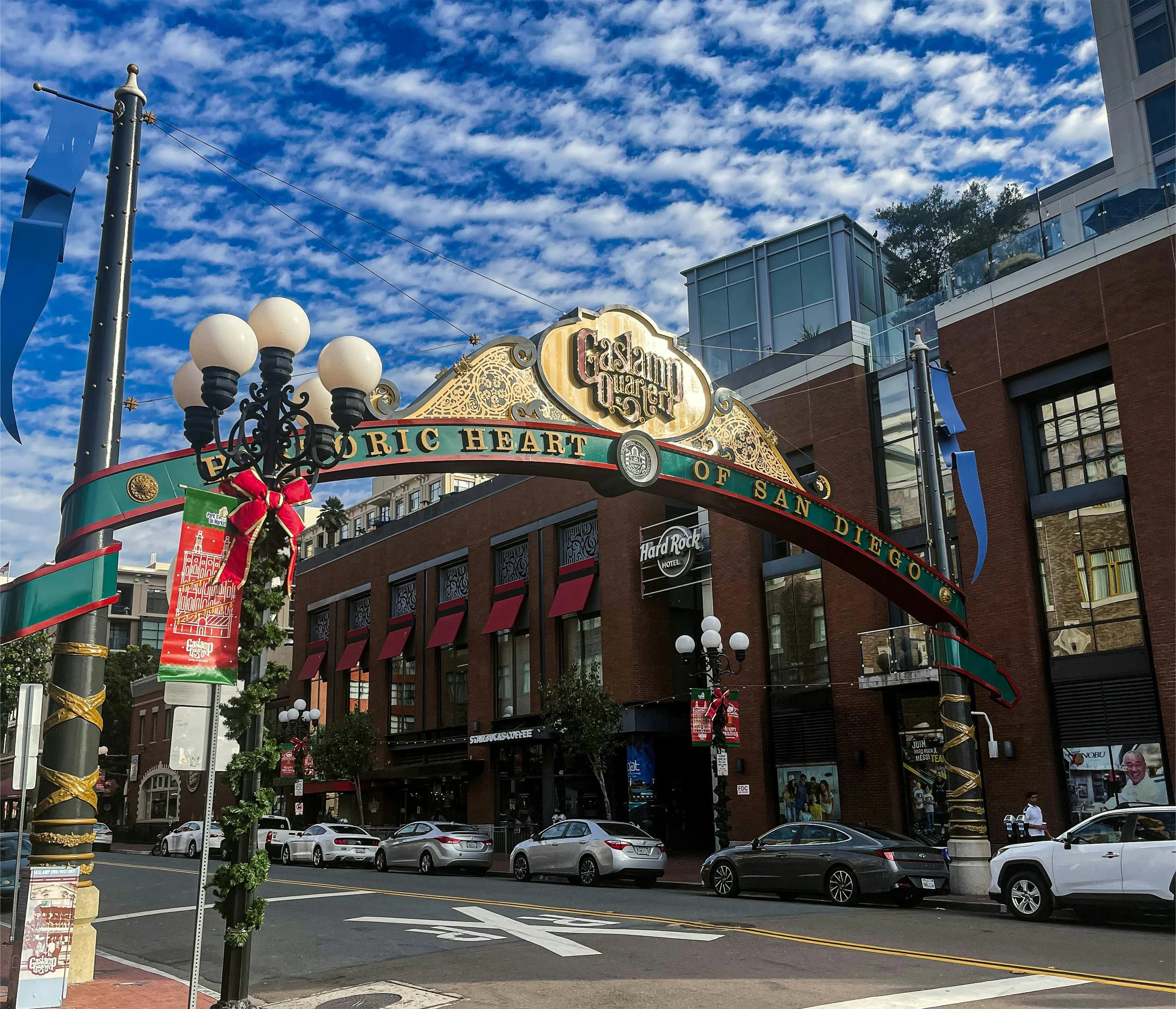The historic Gaslamp Quarter archway, with a sign that says "Historic Heart of San Diego", spans a city street with cars and people.