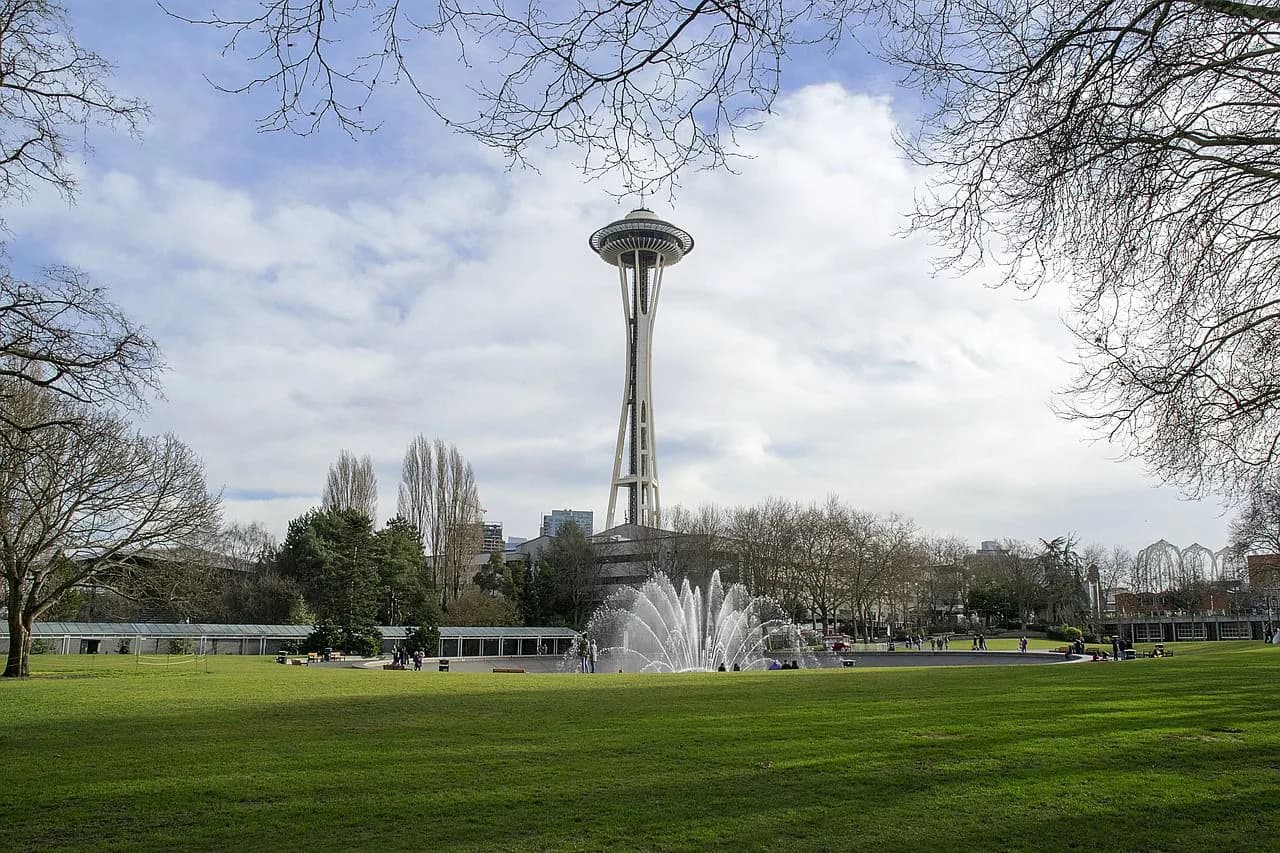 The iconic Space Needle and a water fountain are the centerpiece of a large, green park in Seattle.