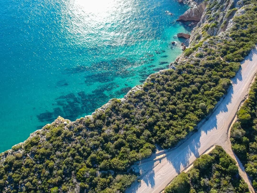 A scenic road winds along a rugged, rocky coastline with the turquoise water of the sea below.