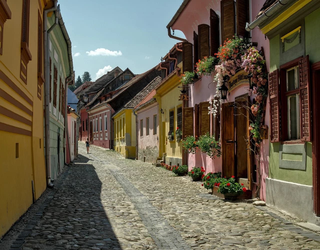 A cobblestone street in Sighisoara is lined with colorful, historic buildings with blooming flowers on the balconies.
