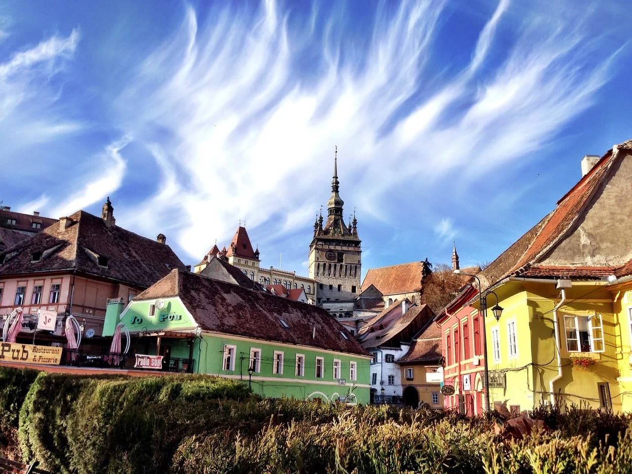 A colorful row of traditional houses with a backdrop of a medieval clock tower and castle creates a fairy-tale scene.