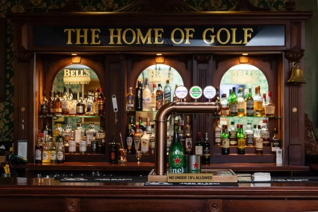 The cozy and elegant interior of a traditional Scottish pub, with a bar that has a sign that says "The Home of Golf".